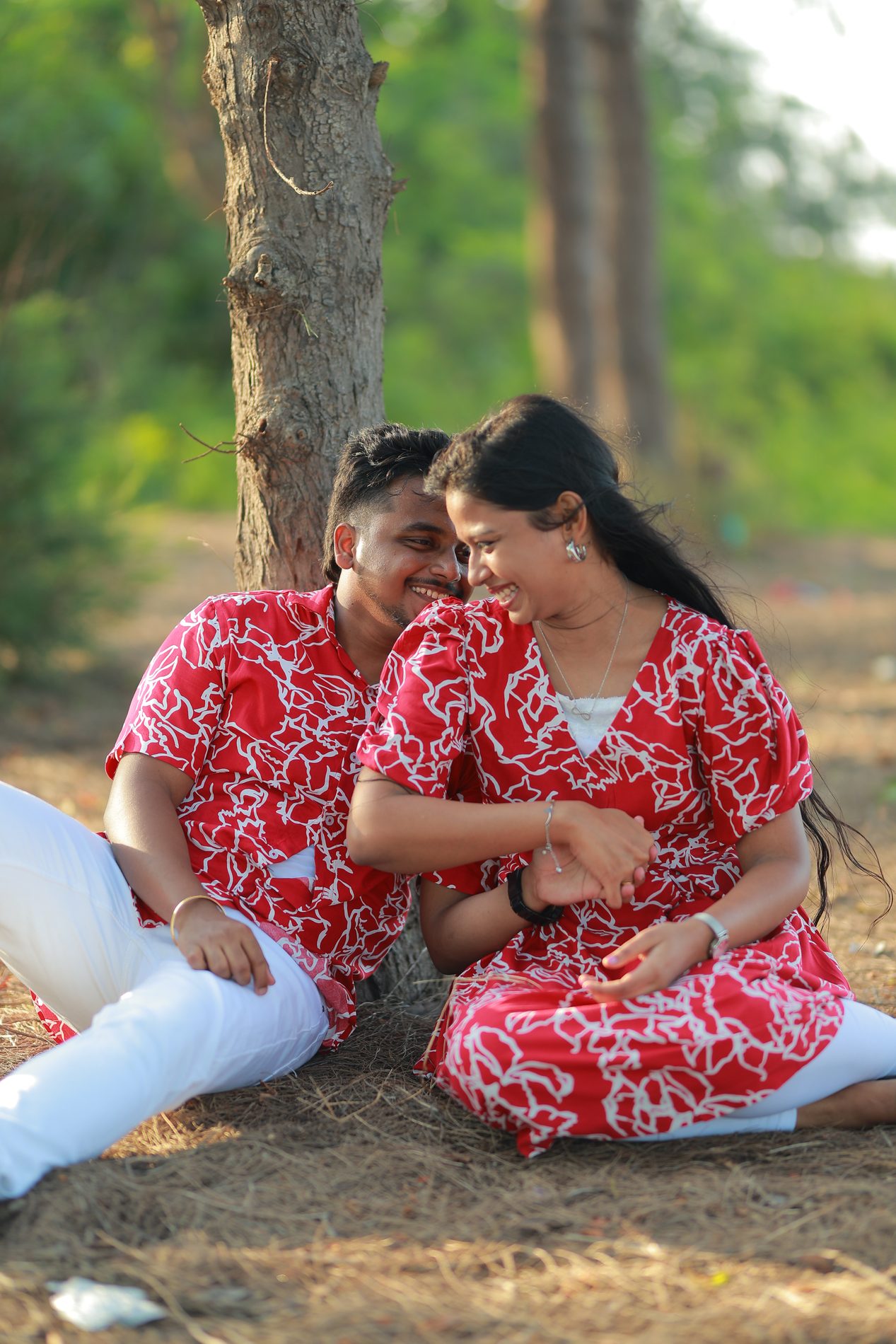 Venkatesh and Brindha laughing together on a fallen log in the woods