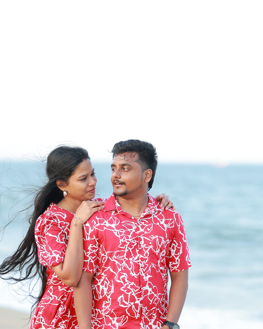 Venkatesh and Brindha together on the beach, ocean behind them